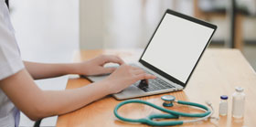 Healthcare Worker Typing on Laptop Next to Stethoscope